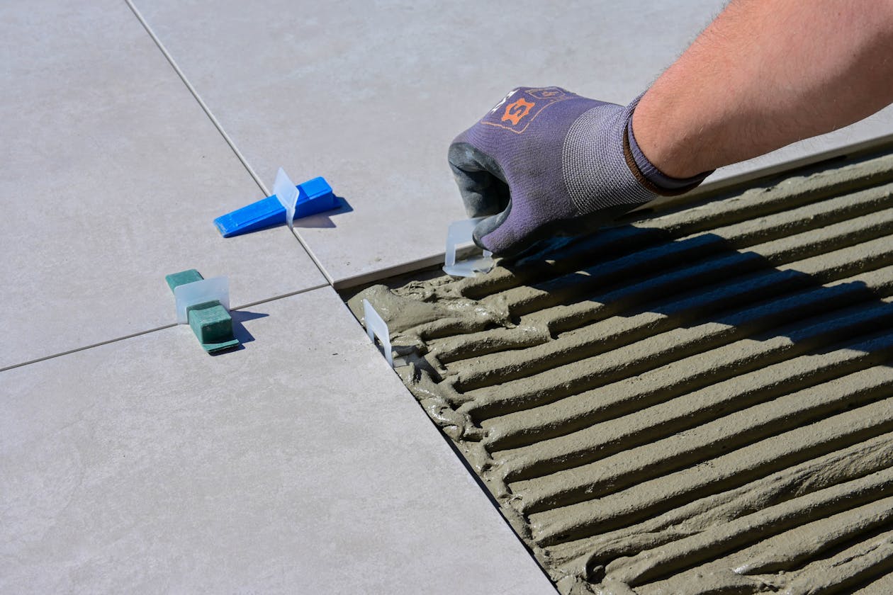 Detailed view of gloved hand aligning tiles with levelers and spacers during construction. — epoxy flooring contractor Omaha