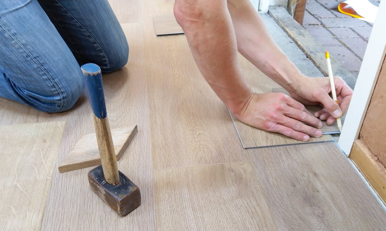 A craftsman carefully measures and marks wooden floor panels for precise installation. — epoxy garage floor cost
