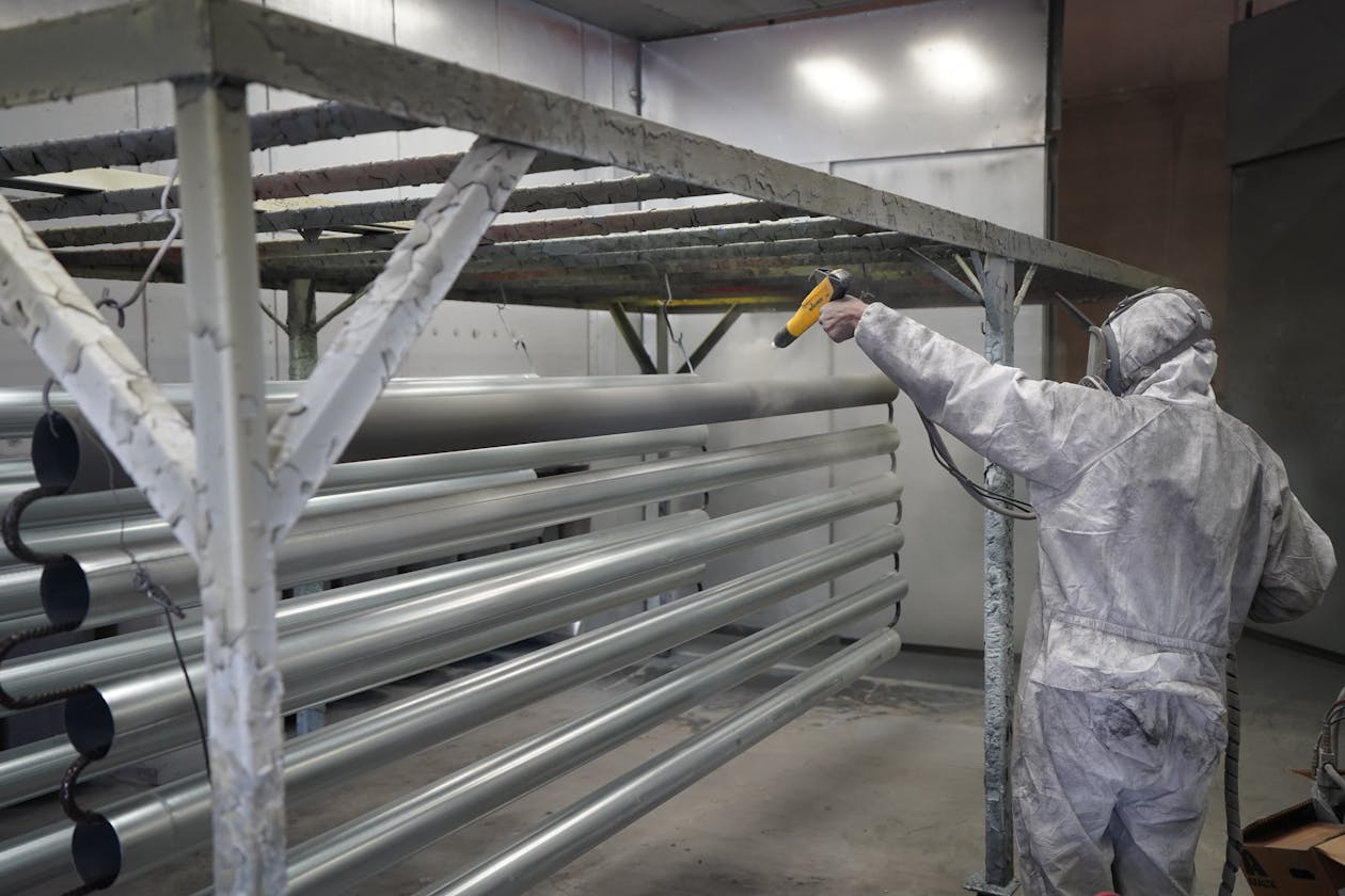 Technician applying powder coating to metal pipes in a workshop setting. — anti-slip epoxy coating