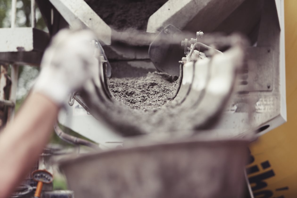 Close-up of concrete being poured from a mixer truck at a construction site with a worker's hand visible. — decorative concrete overlay